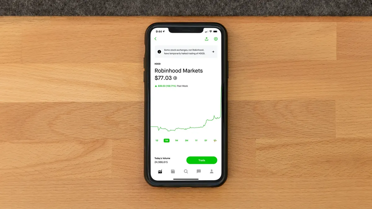 Stock trading app on smartphone displaying Robinhood Markets price on wooden desk.