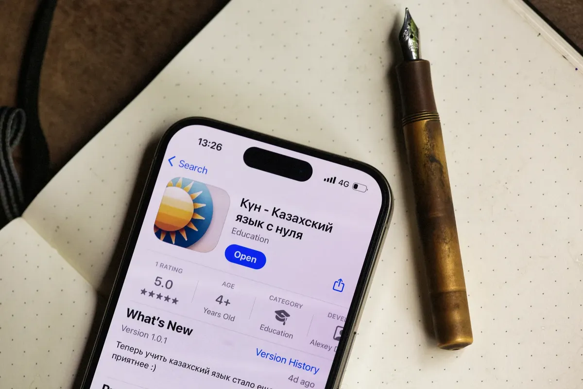 Smartphone displaying a language learning app next to a vintage pen on a notebook.