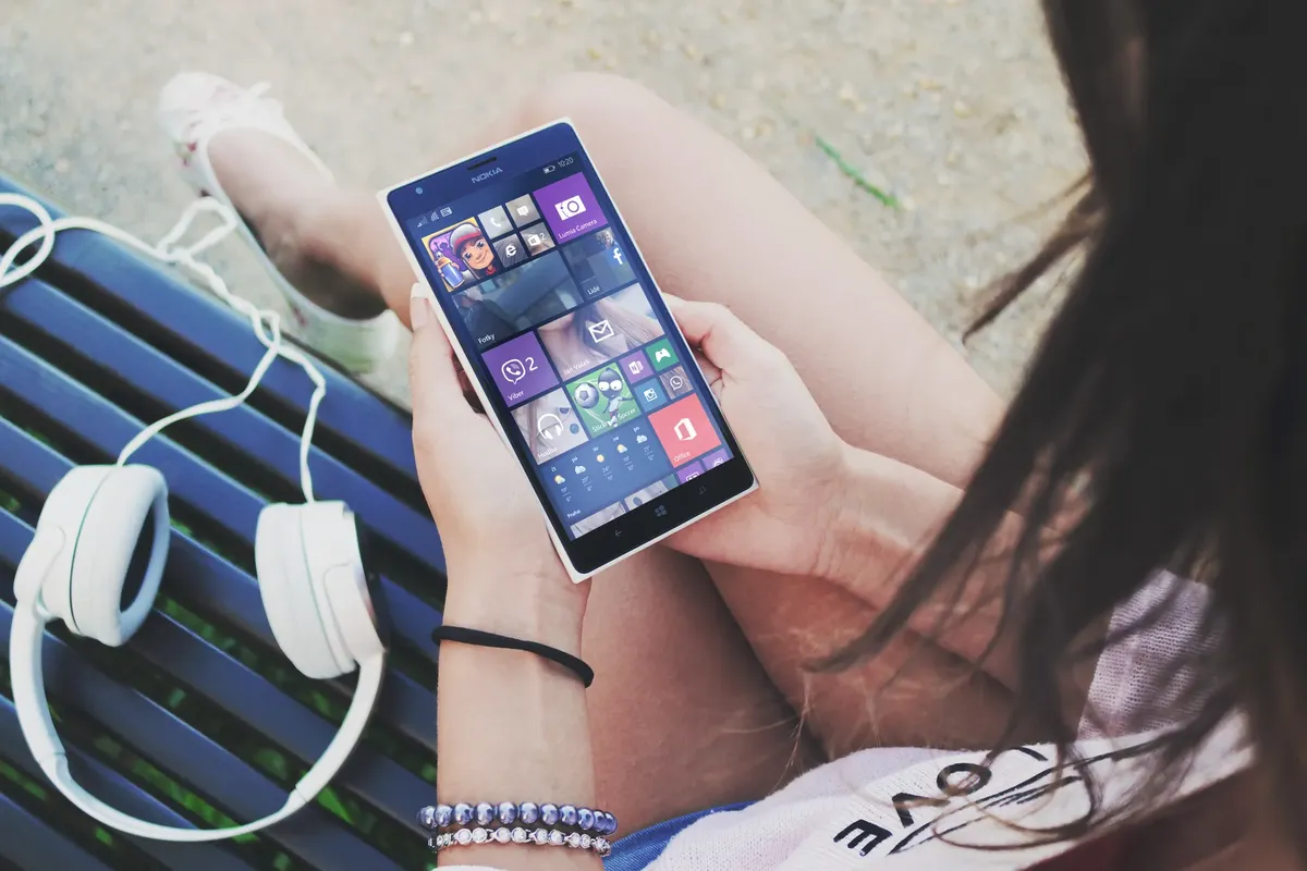 Close-up of a woman using a Windows smartphone with headphones outdoors.